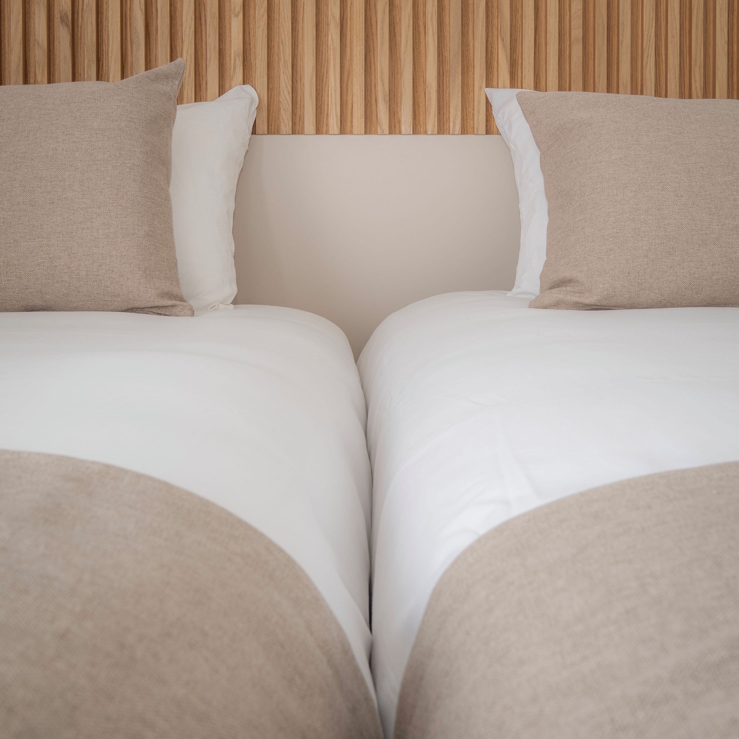 Una cama doble con dos almohadas, cabecera de madera y pared lisa.