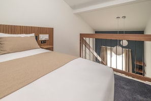 A bedroom with a large bed, wooden headboard, a nightstand with a radio, and a view of a staircase leading to a balcony. - Hotel le Relais des Brasseurs (Aubagne)