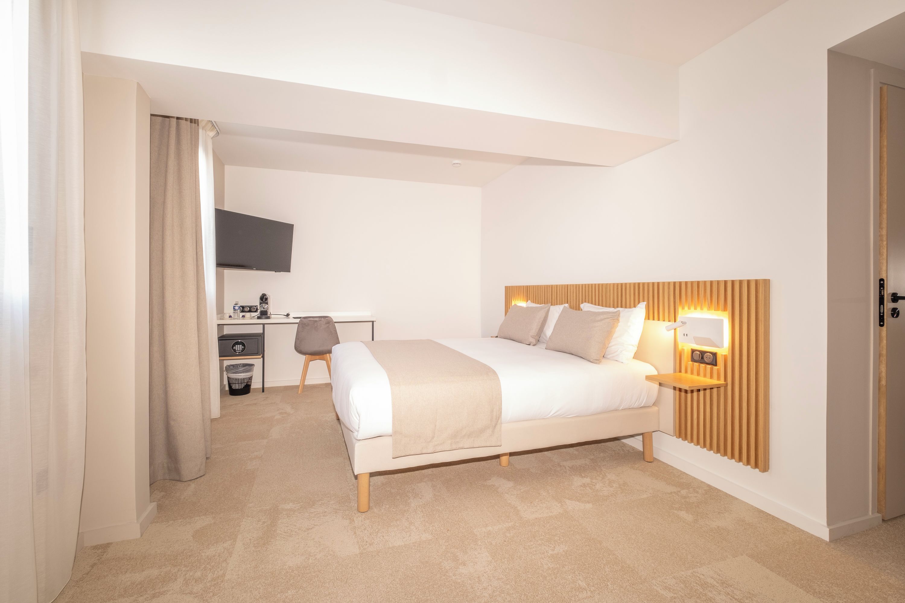 A modern hotel room with a bed, bedside table, and a desk with a chair.
