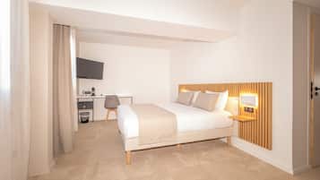 A modern hotel room with a bed, bedside table, and a desk with a chair.