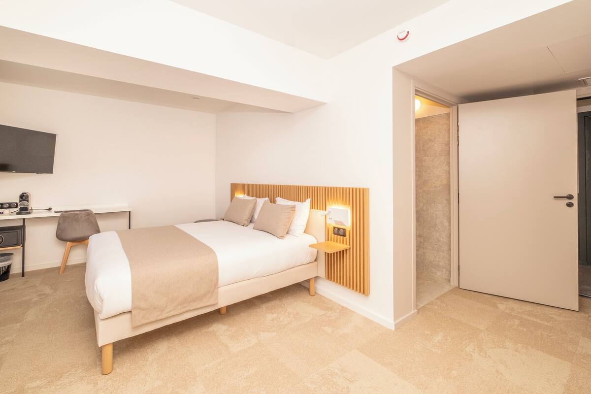 A modern bedroom with a bed, bedside table, and a desk with a chair.