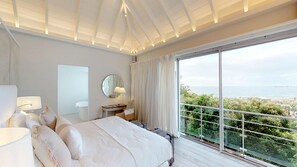 A bedroom with a large bed, a bedside table, a mirror, and a view of the sea. - Le Toiny (St. Barthelemy)
