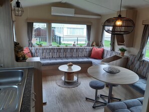 Ein kompakter Wohnbereich mit Küchenzeile, einer Couch, einem Esstisch und einem großen Fenster mit Blick ins Freie.