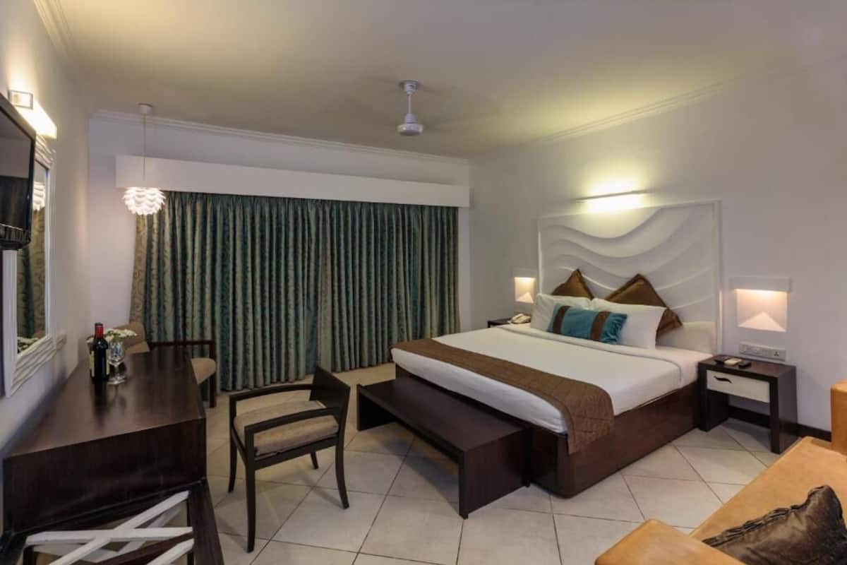 A hotel room with a bed, bedside tables, a desk, a chair, and a bench.