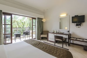 A hotel room with a bed, a desk, a chair, a television, and a balcony with chairs and curtains. - Sonesta Inns Beach Resort - Candolim Beach (Candolim)