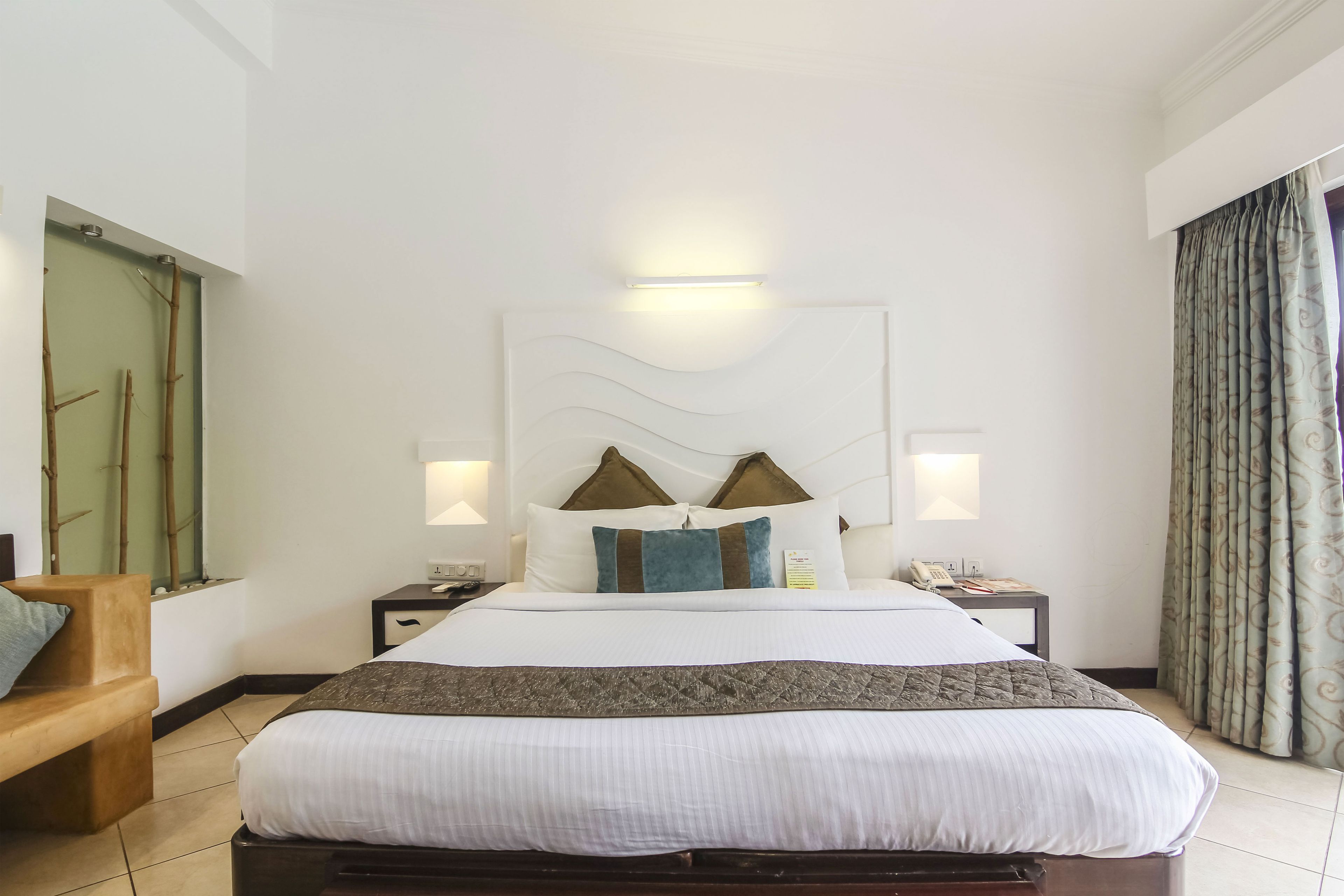 A hotel room with a bed, bedside lamps, a nightstand, a chair, and a window with curtains.