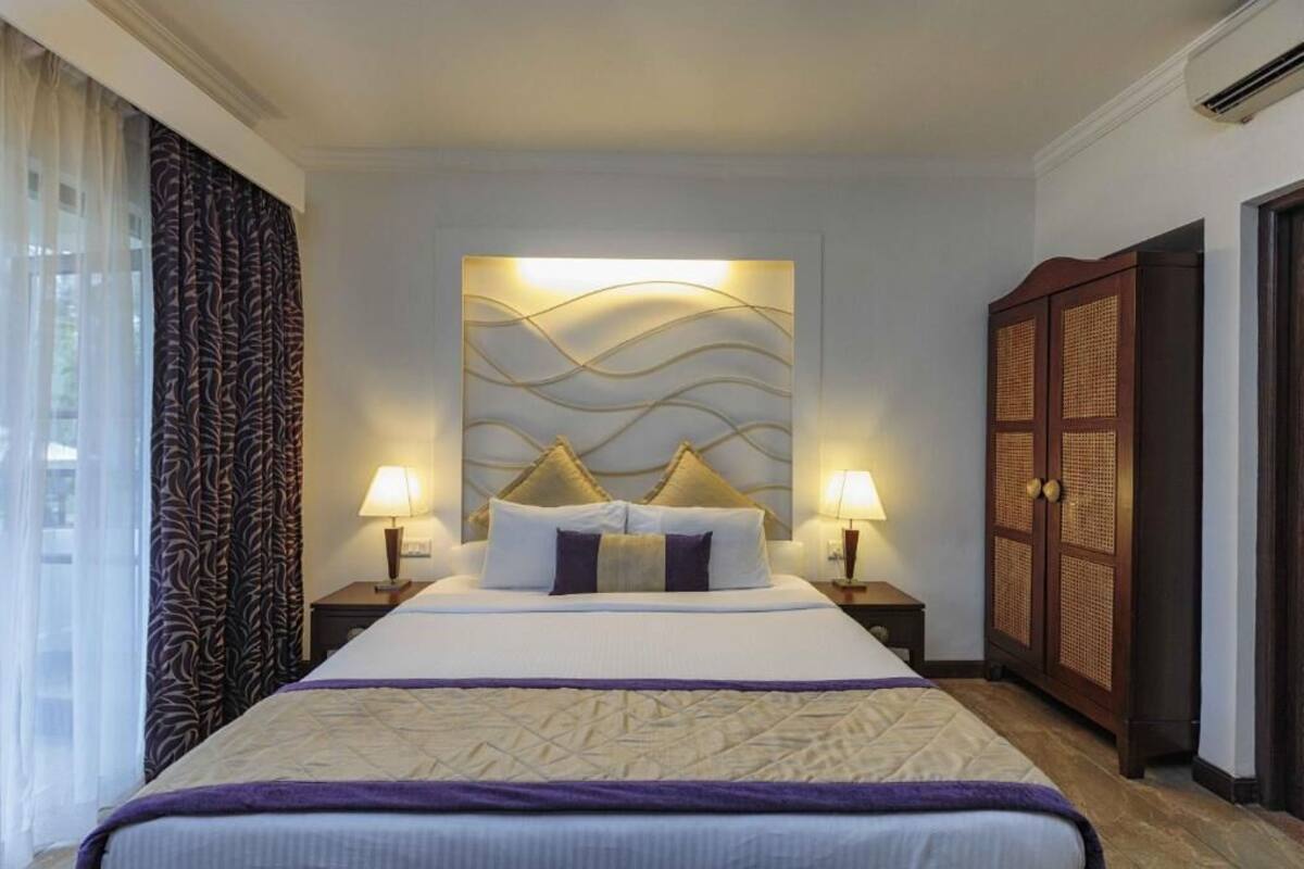 A hotel room with a large bed, two bedside lamps, a decorative headboard, and a wardrobe.