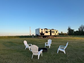A recreational vehicle (RV) with a kitchen area, a dining table, and four Adirondack chairs in a grassy field.