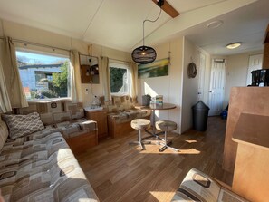 A cozy RV interior with a sofa, a small table, and a hanging light fixture. - DD 45 - Camping de Duindoorn - Airco by Interhome (IJmuiden)