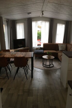 Ein modernes Wohnzimmer mit einer Couch, einem Fernseher, einem Esstisch mit Stühlen und einem kleinen runden Tisch mit Pflanze.