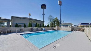 Une piscine avec une plage en béton, un bâtiment portant une enseigne « Best Western », et un ciel bleu dégagé.