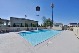Una piscina con plataforma de hormigón, un edificio con un cartel que dice 'Best Western' y un cielo azul despejado.