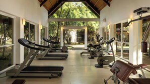 Academia com esteiras, bicicletas ergométricas e equipamentos de ginástica sob um teto de madeira com grandes janelas.