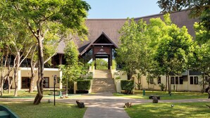 Um edifício com uma escadaria central, rodeado por árvores e um caminho.