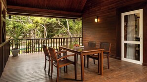 Um deck de madeira com mesa e cadeiras, um vaso de planta e vista para árvores.