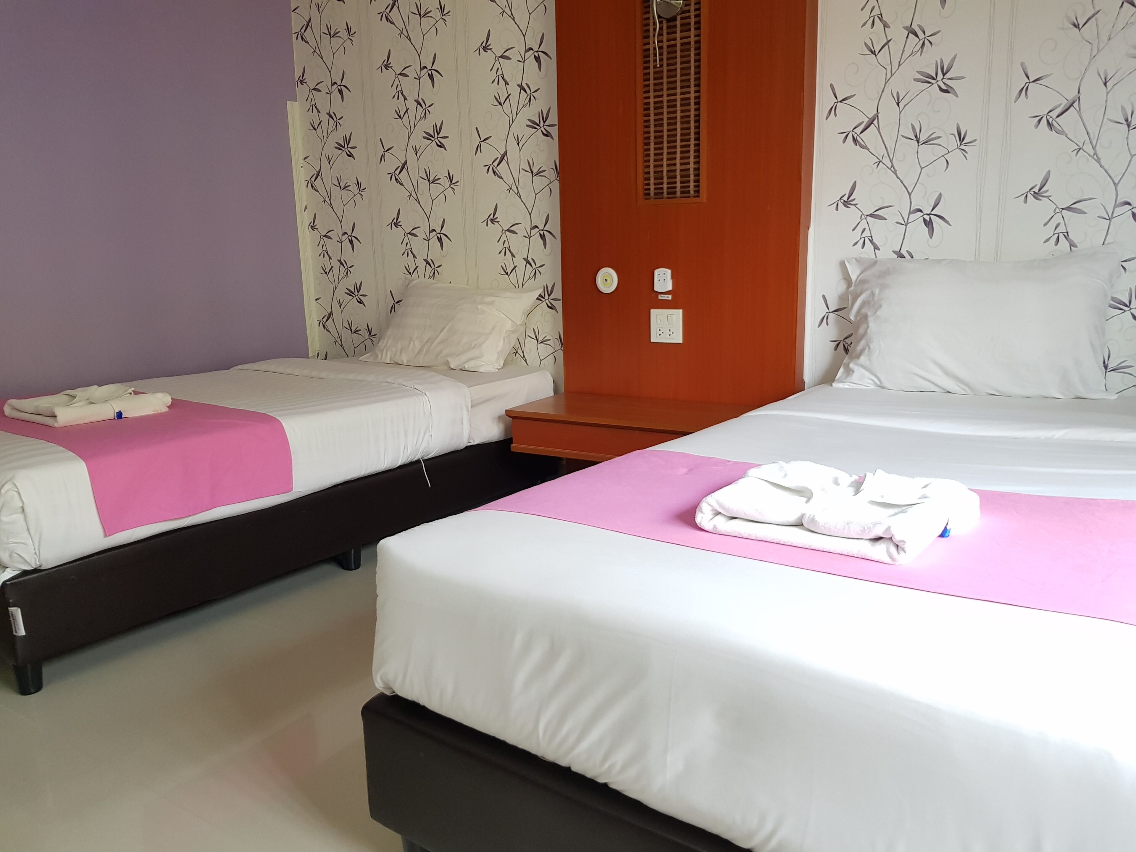 Ein Hotelzimmer mit zwei Betten, einem Holzschrank, einem Badezimmer mit Spiegel und einer Wand mit Blumenmuster.