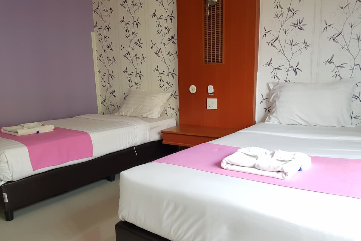 A hotel room with two beds, a wooden wardrobe, a bathroom with a mirror, and a wall with a floral pattern.