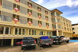Um hotel de vários andares com fachada marcante, apresentando padrões verticais em branco e rosa. Vários veículos estão estacionados em frente ao edifício.