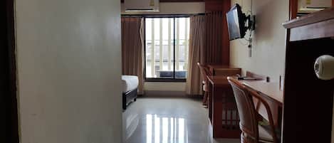 A hotel room with a bed, a desk with chairs, a television, and a window with curtains.