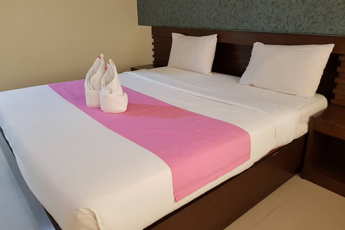 Uma cama bem arrumada com lençóis brancos e um toque de cor rosa, uma cabeceira de madeira e um par de chinelos sobre a cama.