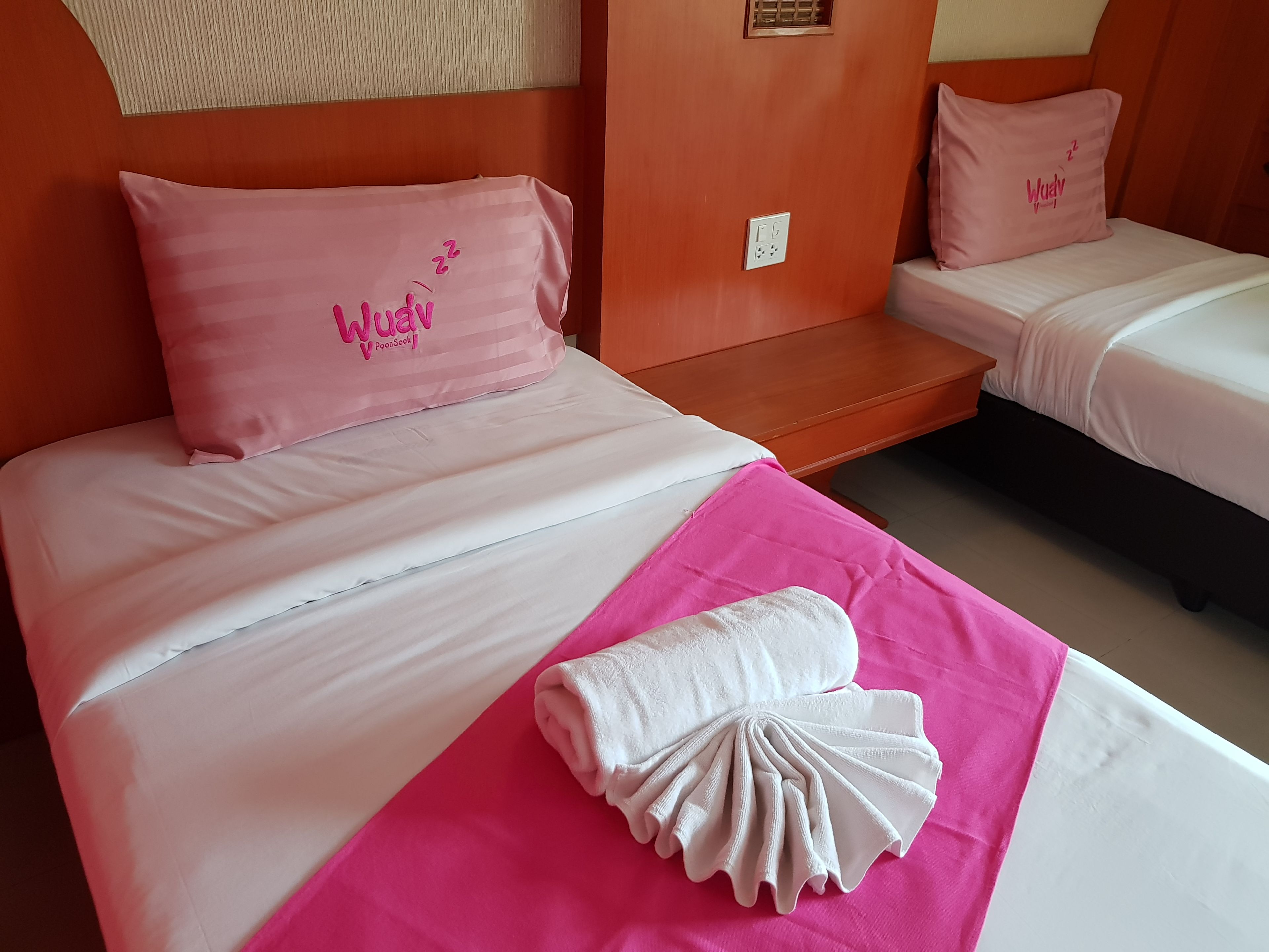 Une chambre d’hôtel avec deux lits, chacun agrémenté d’un oreiller rose et d’une couverture blanche. On peut voir une serviette rose sur le lit, au premier plan.
