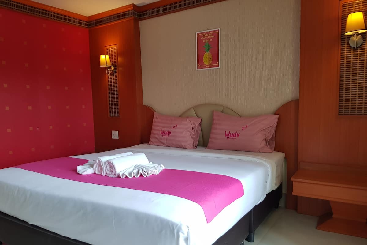 Quarto de hotel com uma cama, almofadas, uma luminária de parede e um cartaz.