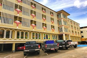 A multi-story hotel with a distinctive facade featuring vertical white and pink patterns. There are several parked vehicles in front of the building. - Poonsook Phitsanulok Hotel SHA Plus+ by Zuzu (Phitsanulok)