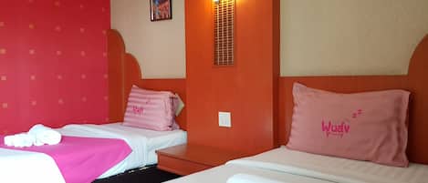 Quarto de hotel com duas camas, cada uma com uma almofada rosa e uma toalha branca. Há um quadro na parede e um aplique.