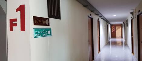 A hallway with a fire exit sign, a phone number sign, and a door marked with the number 1.