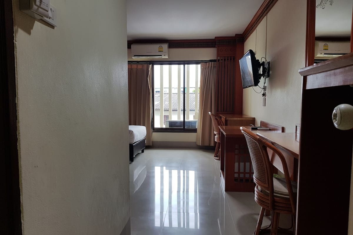A hotel room with a bed, a desk with chairs, a television, and a window with curtains.