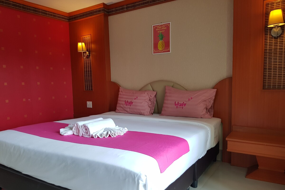 A hotel room with a bed, pillows, a wall-mounted lamp, and a poster.