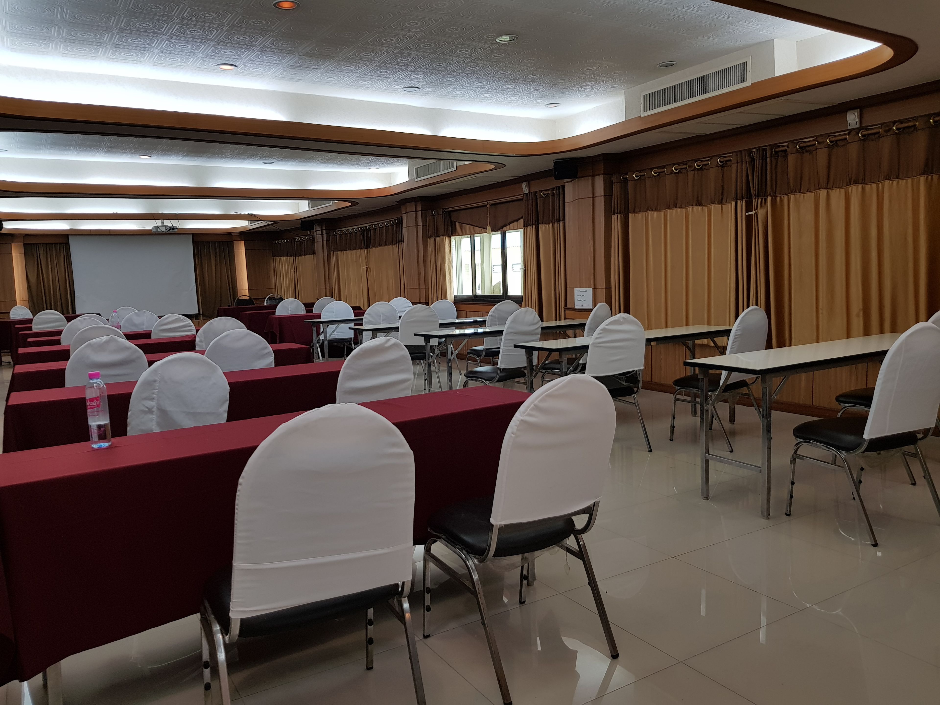 A conference room with rows of tables and chairs, a projector screen, and a large window.