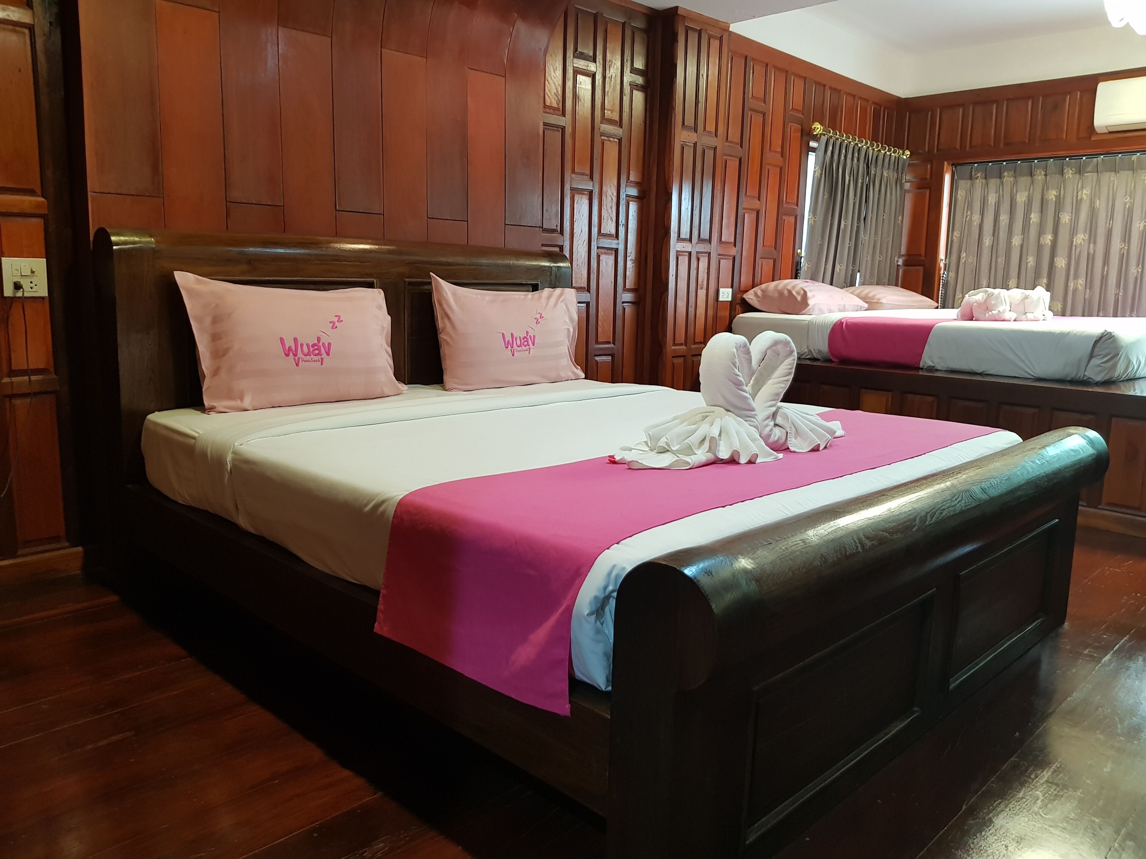 Ein Hotelzimmer mit einer Wandpaneelaus Holz, einem Bett mit rosa Bettwäsche und Kissen sowie einem weiteren Bett im Hintergrund.