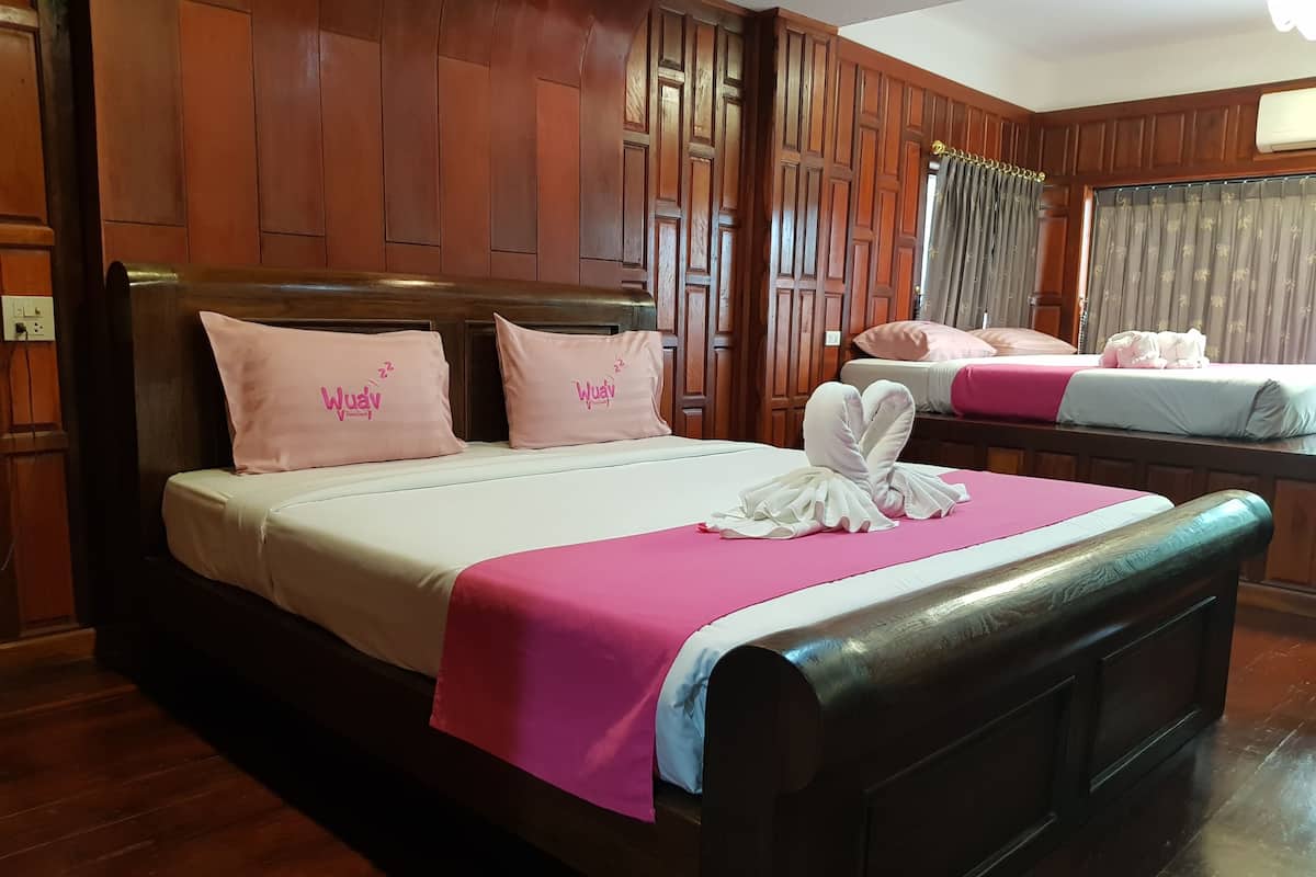 A hotel room with a wooden paneled wall, a bed with pink bedding and pillows, and a second bed in the background.
