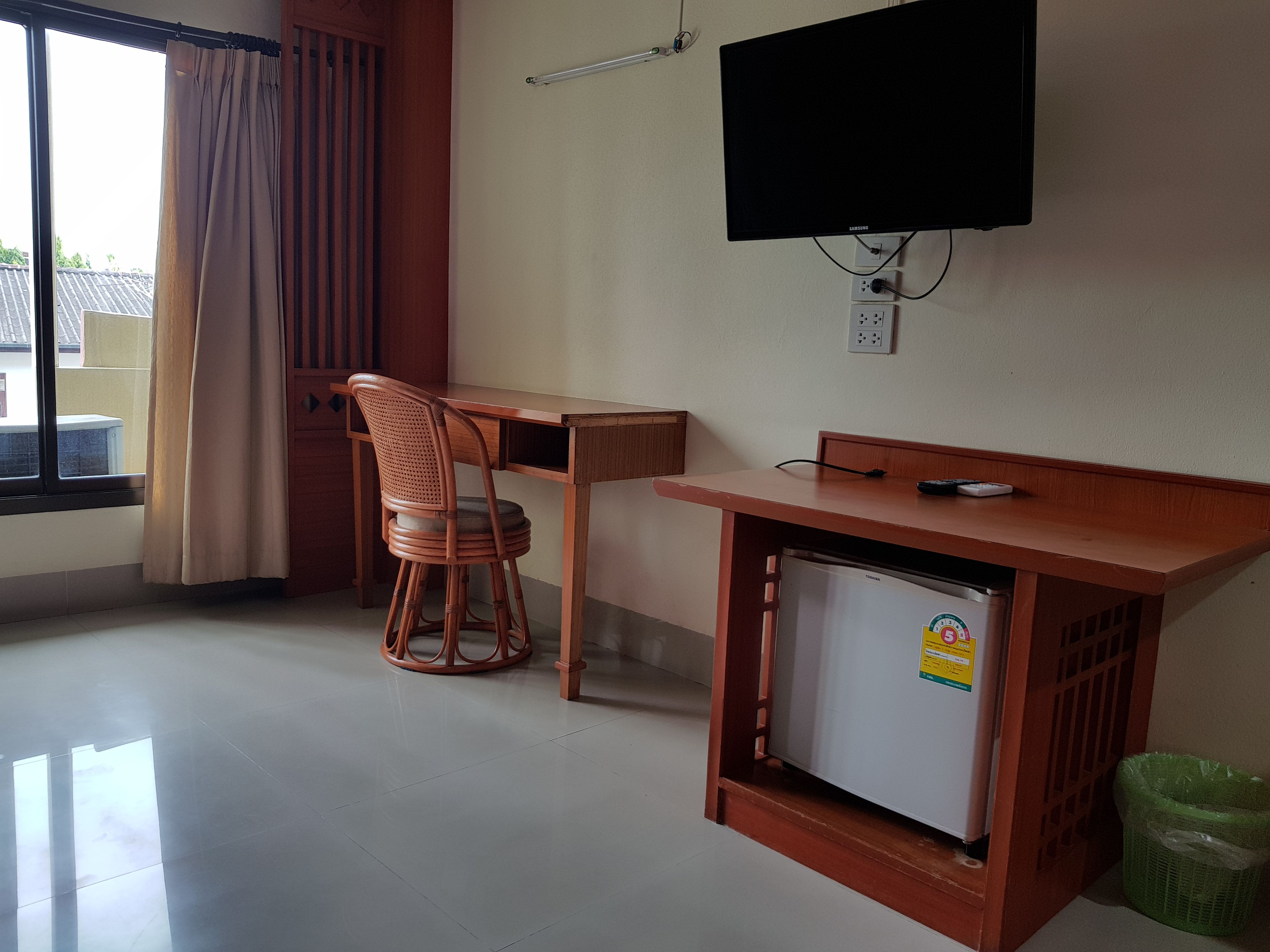 A room with a wooden desk, a chair, a television mounted on the wall, and a small refrigerator.