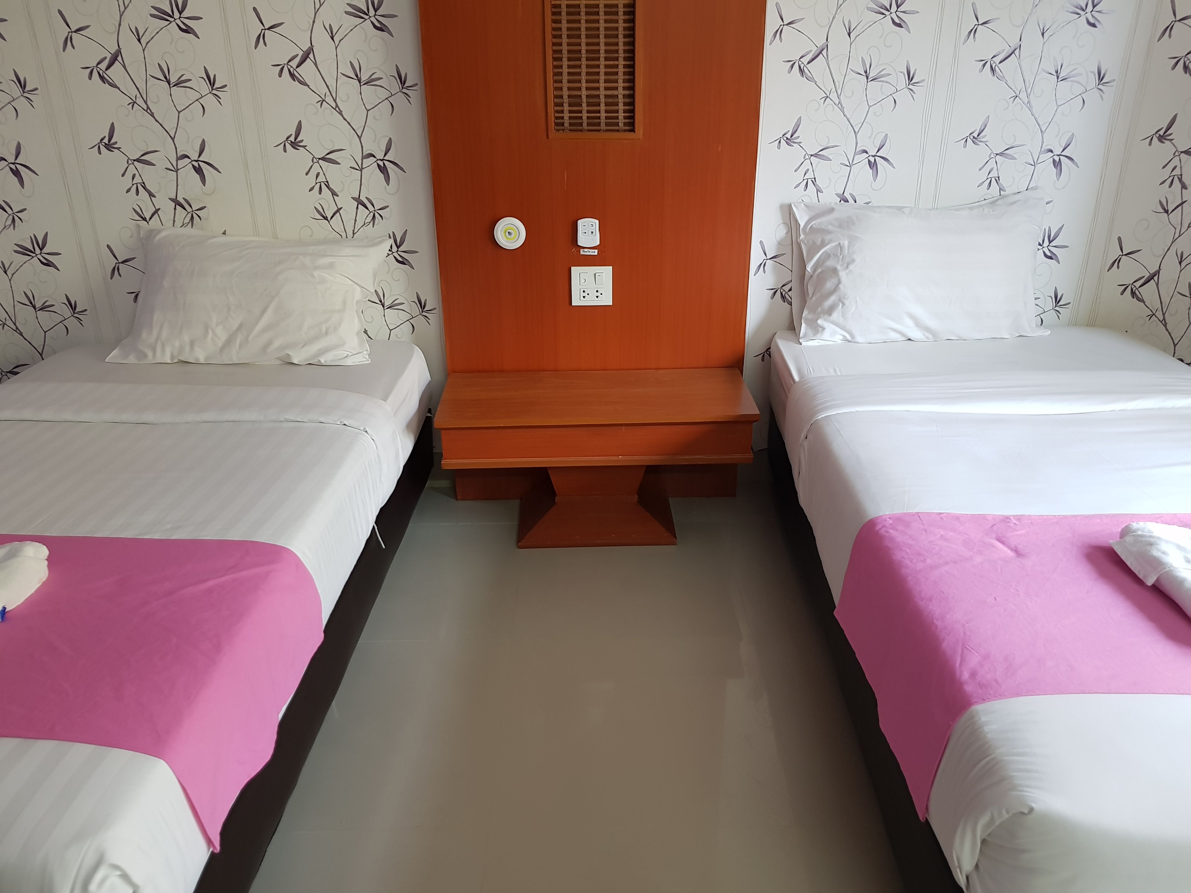 Ein Hotelzimmer mit zwei Einzelbetten, einem Holznachttisch und einem an der Wand montierten Heizgerät.