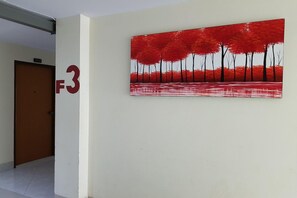 Um corredor com uma porta marcada '312' e um quadro grande, em vermelho e preto, na parede.