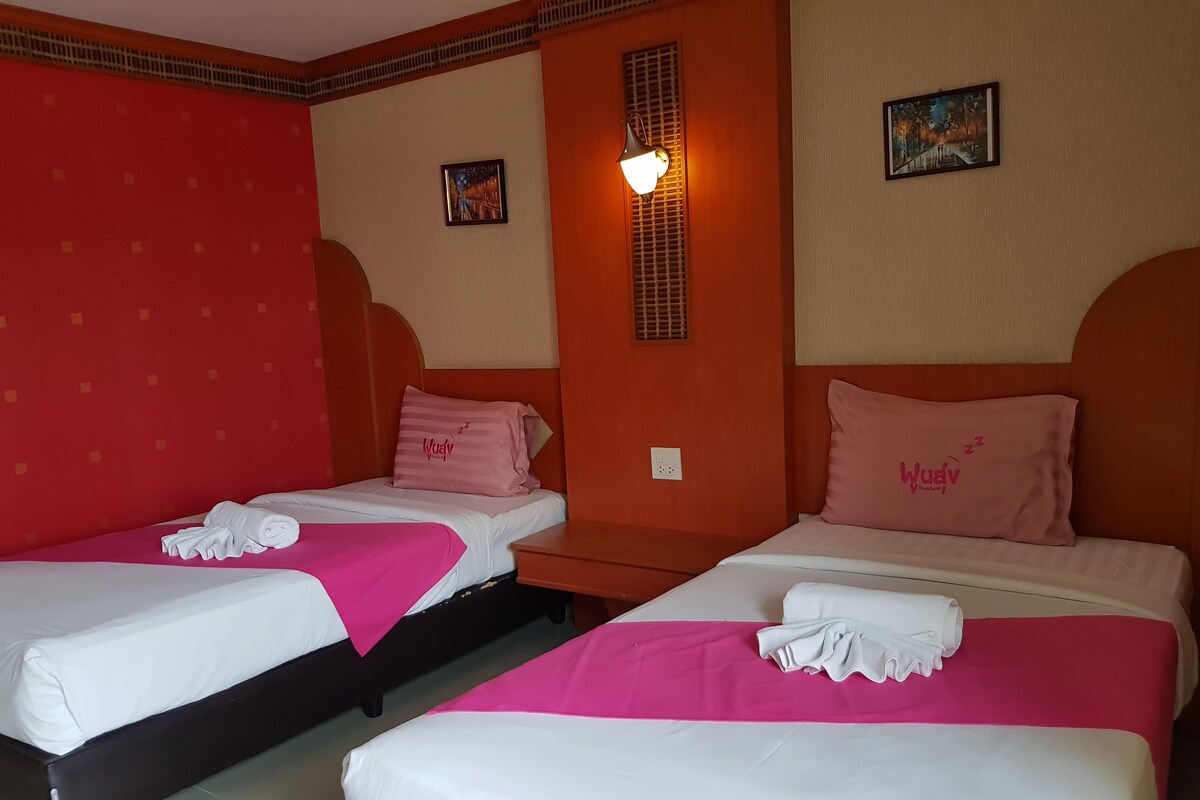 A hotel room with two beds, each with a pink pillow and a white blanket.