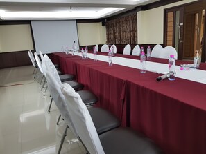 Uma sala de conferências com uma mesa comprida, cadeiras, garrafas de água e uma tela de projetor.
