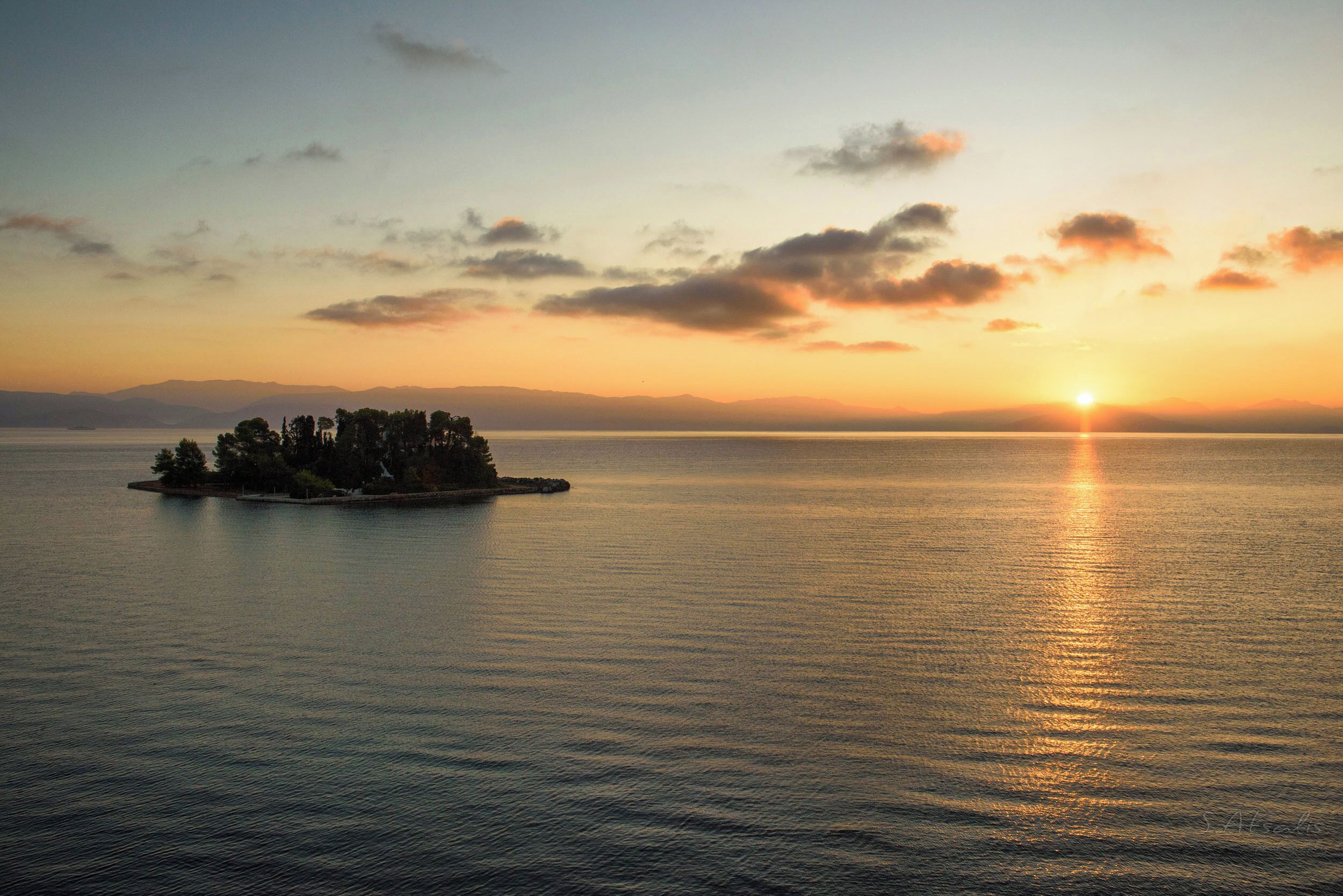 A calm body of water with a small island and distant mountains.