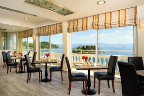 Un restaurant avec des tables et des chaises, de grandes fenêtres offrant une vue sur un lac et des montagnes, et un balcon doté d’une balustrade.