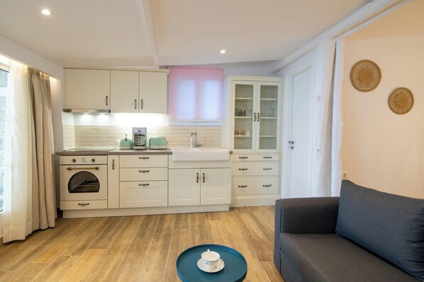 A compact kitchen with a built-in oven, a sink, and a dining area with a sofa. - Pontikonissi Adults Only (Corfu)