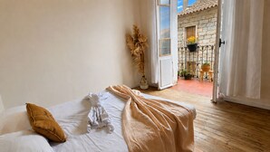 Un dormitorio con cama, ventana y vista a un balcón exterior con plantas en macetas.