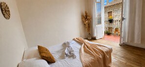 A bedroom with a bed, a window, and a view of an outdoor balcony with potted plants.