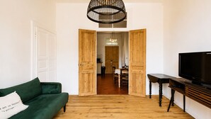 Una sala de estar con un sofá verde, un mueble bajo de madera para televisor y un área de comedor al fondo.