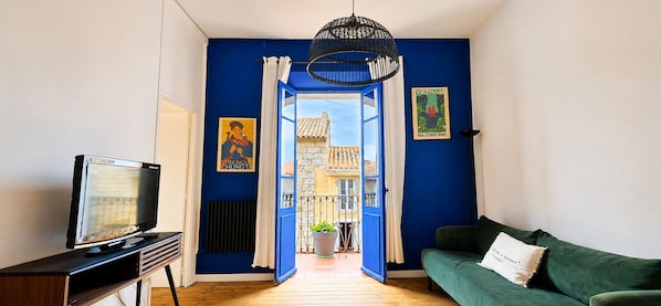 A room with a TV, a green sofa, a blue wall, a door leading to a balcony, and a hanging light fixture.