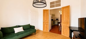 A living room with a green sofa, a TV, and wooden doors leading to a kitchen.