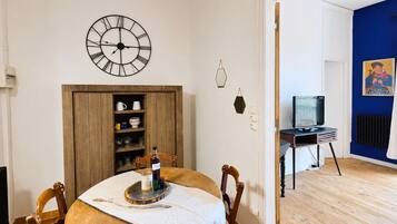 Een kamer met een eettafel, stoelen, een wandklok, een televisie en een blauwe accentmuur.