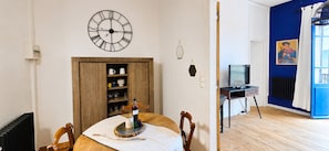 A room with a dining table, chairs, a wall clock, a television, and a blue accent wall.