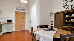 Cocina compacta con microondas, horno y puerta de madera. Hay una mesa de comedor con sillas y un reloj en la pared.